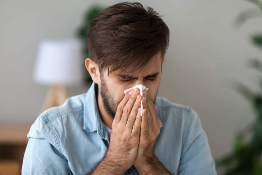 Man covering his mouth and nose while sneezing due to allergy